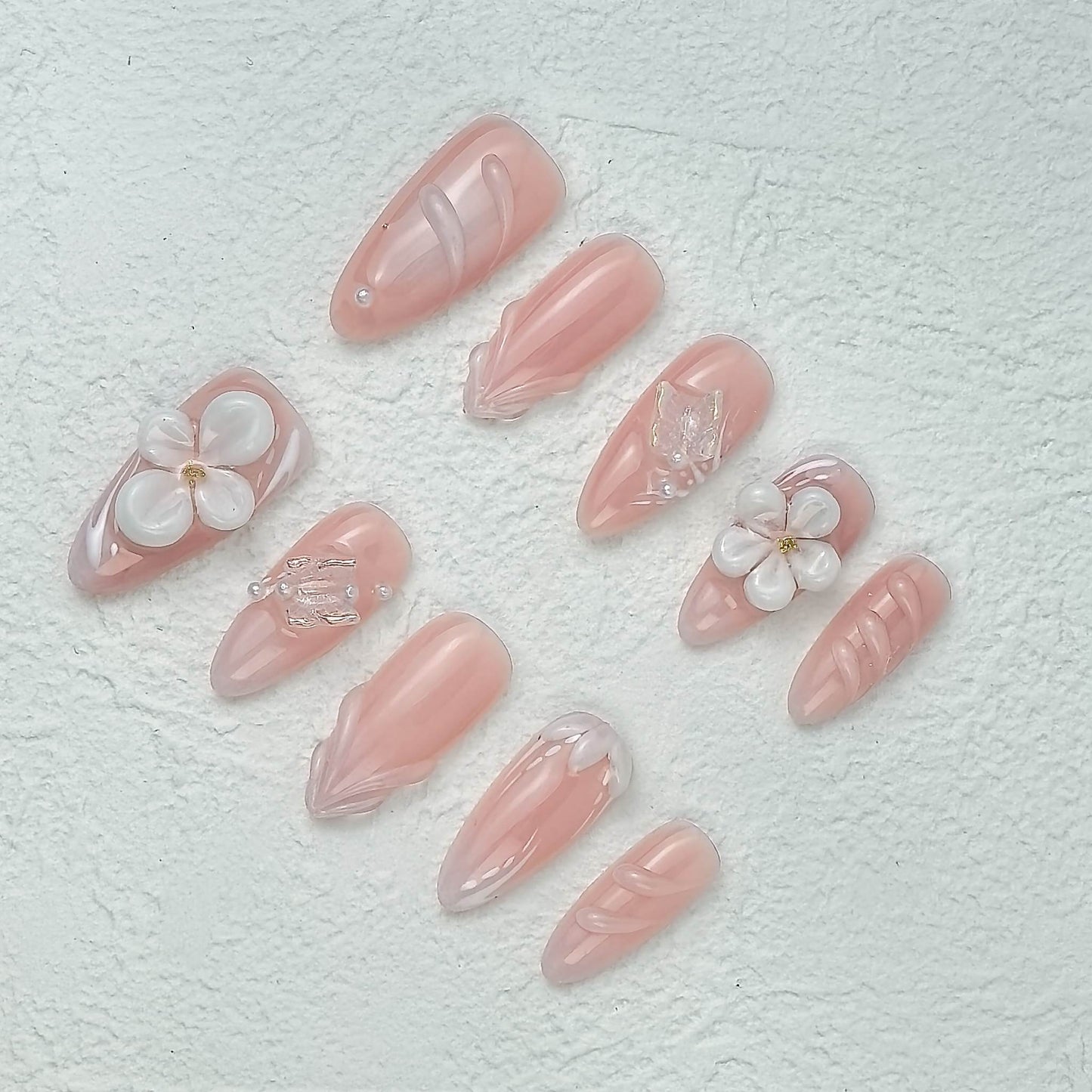 Pink floral press-on nails displayed at an angle on white textured background