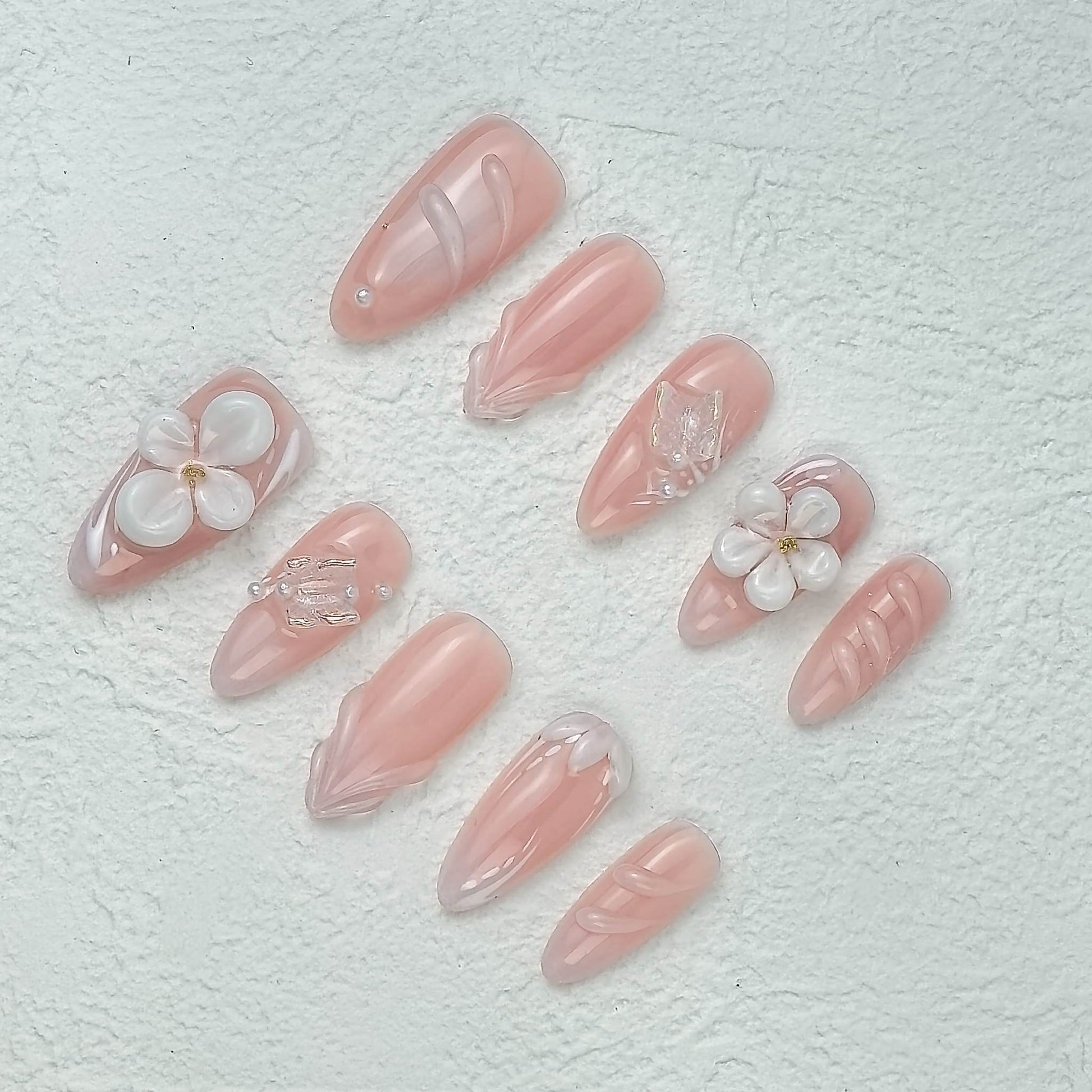 Pink floral press-on nails displayed at an angle on white textured background